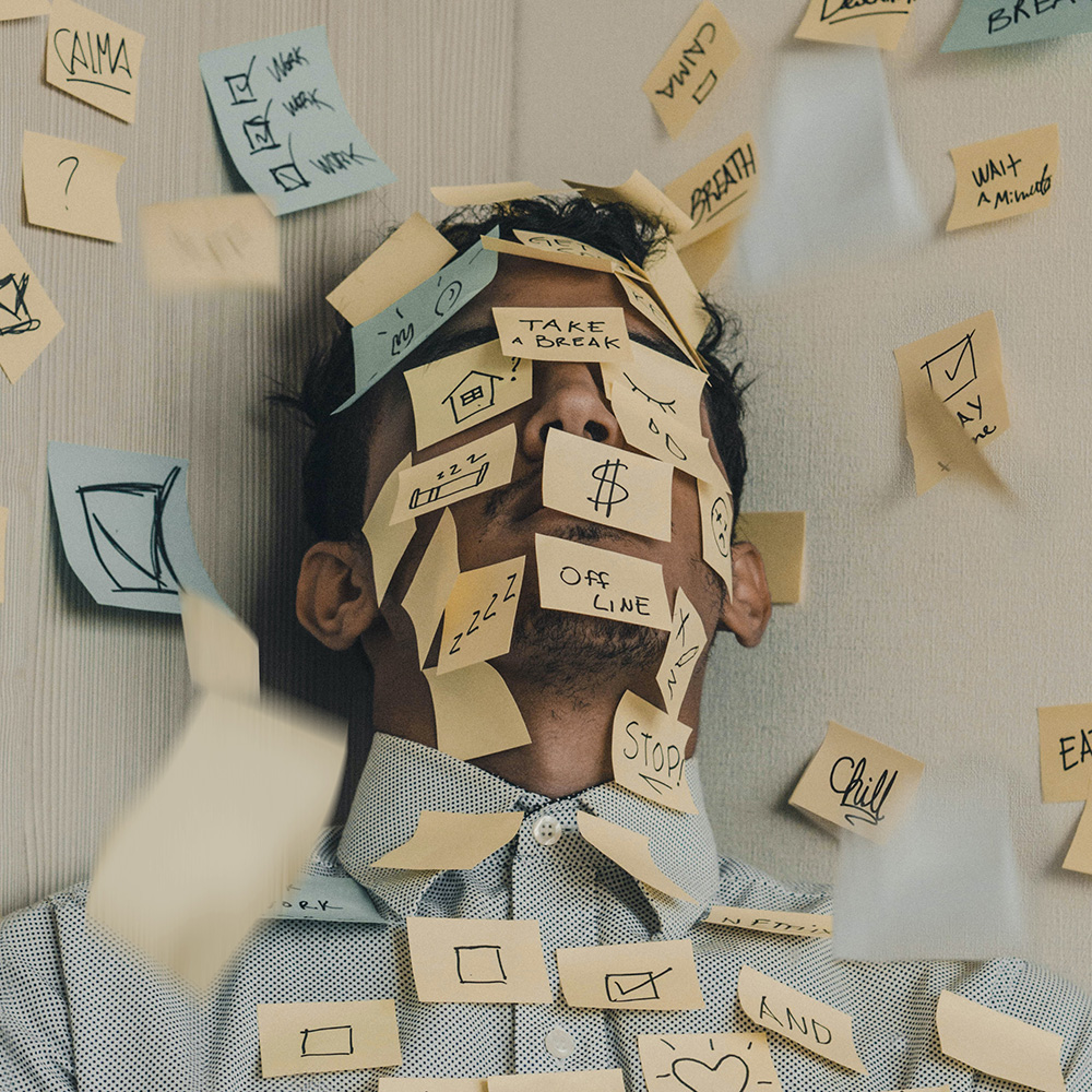 Young man with post-it notes on his face, feeling overwhelmed and in need of burnout coaching