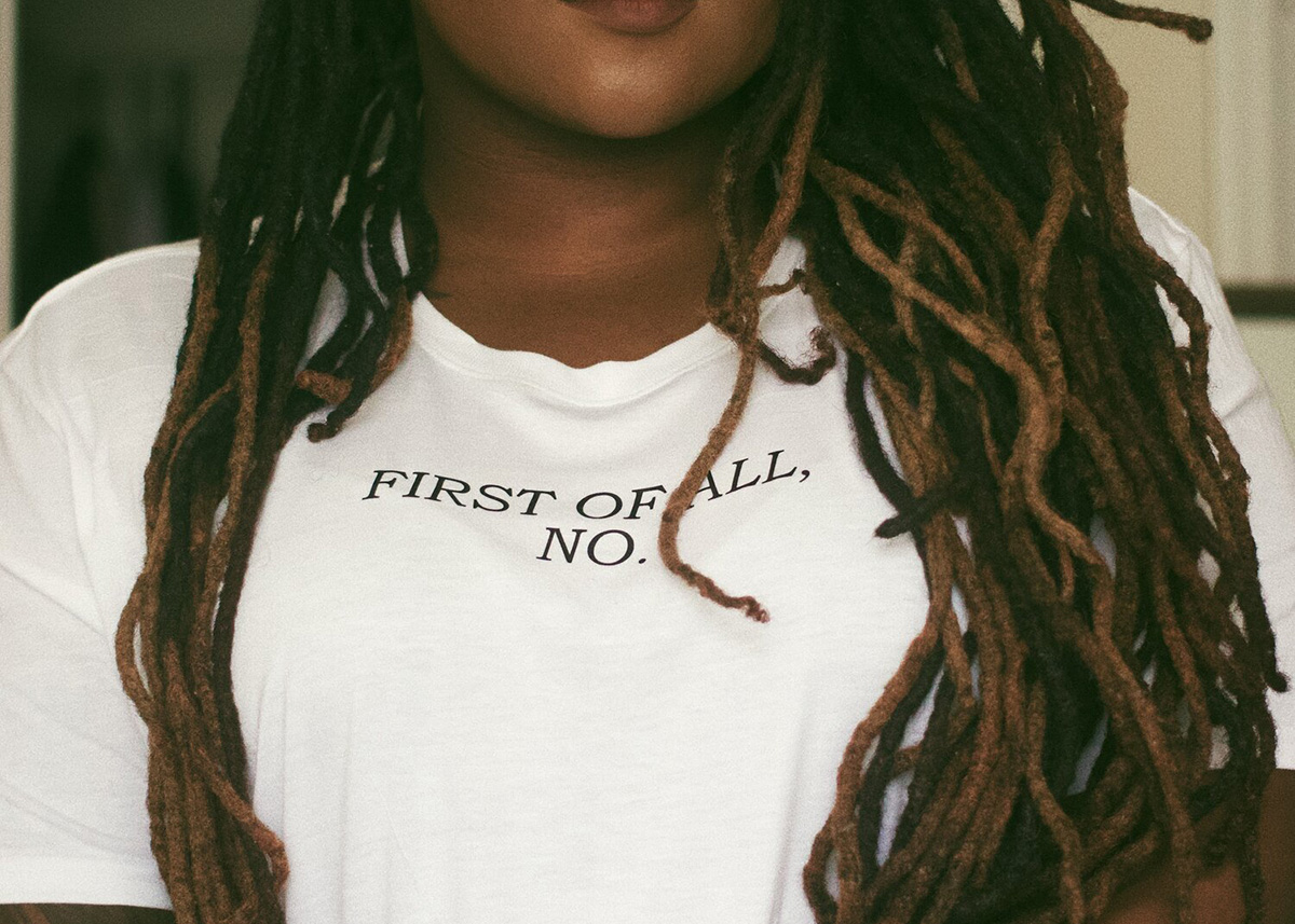 Black woman wearing "first of all no" t-shirt. The discourses that fuel burnout do not affect everyone equally.