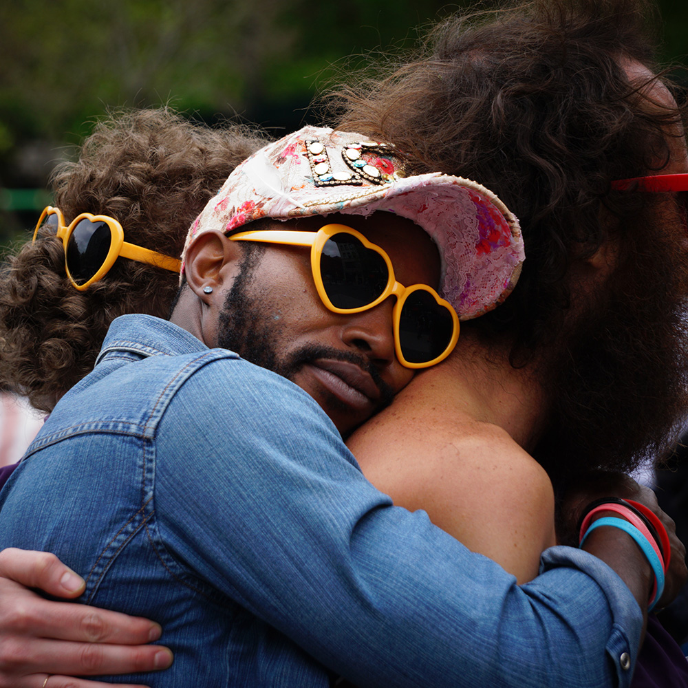 Black man with heart shaped sunglasses hugging his partner. Therapy for LGBTQIA+ in St. Louis with Kathryn Stinson, LPC